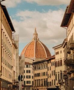 Charming street view of Florence showcasing the famous Duomo dome under a partly cloudy sky.